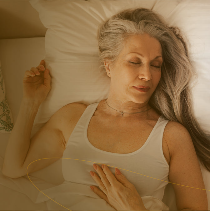 Woman lying in bed wearing a white tank top with a warm, soft light.